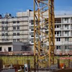 Canteiro de obras com um guindaste ao lado de um edifício em construção sob céu claro.