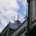 Caixa-d’água instalada no topo de uma edificação contra um céu azul com nuvens.