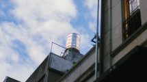 Caixa-d’água instalada no topo de uma edificação contra um céu azul com nuvens.