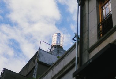 Caixa-d’água instalada no topo de uma edificação contra um céu azul com nuvens.