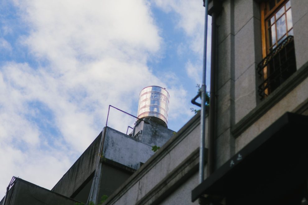 Caixa-d’água instalada no topo de uma edificação contra um céu azul com nuvens.