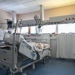Leito de unidade de terapia intensiva cercado por equipamentos médicos modernos em um ambiente hospitalar.