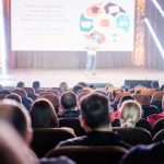 Público acompanha uma apresentação em um auditório durante uma conferência.