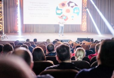 Público acompanha uma apresentação em um auditório durante uma conferência.