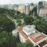 Vista aérea da Praça da Liberdade, em Belo Horizonte, cercada por edifícios de arquitetura neoclássica e áreas verdes.