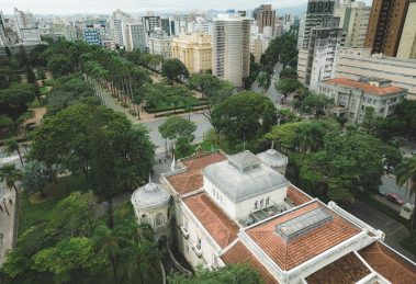 Vista aérea da Praça da Liberdade, em Belo Horizonte, cercada por edifícios de arquitetura neoclássica e áreas verdes.