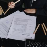 Profissional analisa documentos sobre uma mesa de trabalho, com lápis coloridos ao lado.