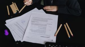 Profissional analisa documentos sobre uma mesa de trabalho, com lápis coloridos ao lado.
