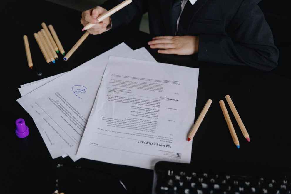 Profissional analisa documentos sobre uma mesa de trabalho, com lápis coloridos ao lado.