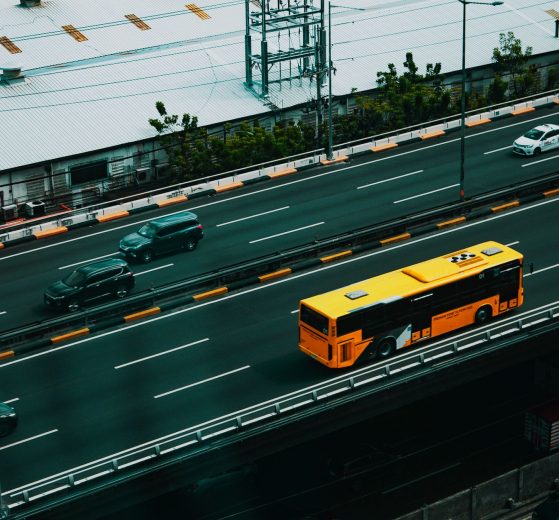 Ônibus urbano amarelo circula por uma avenida movimentada entre carros, visto de cima.