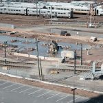 Vista aérea de um canteiro de obras ferroviárias ao lado de trilhos, com trabalhadores e máquinas em operação.