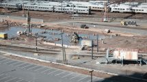 Vista aérea de um canteiro de obras ferroviárias ao lado de trilhos, com trabalhadores e máquinas em operação.
