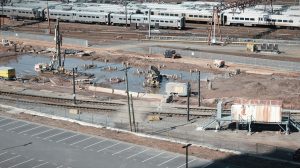 Vista aérea de um canteiro de obras ferroviárias ao lado de trilhos, com trabalhadores e máquinas em operação.