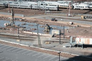 Vista aérea de um canteiro de obras ferroviárias ao lado de trilhos, com trabalhadores e máquinas em operação.