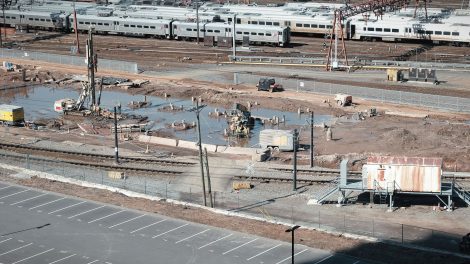 Vista aérea de um canteiro de obras ferroviárias ao lado de trilhos, com trabalhadores e máquinas em operação.