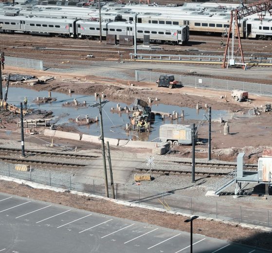 Vista aérea de um canteiro de obras ferroviárias ao lado de trilhos, com trabalhadores e máquinas em operação.