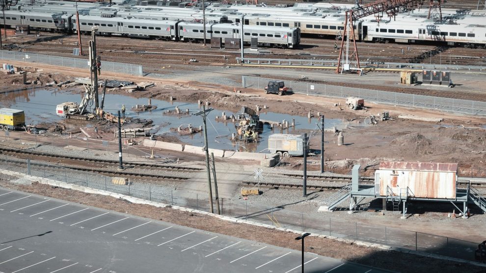 Vista aérea de um canteiro de obras ferroviárias ao lado de trilhos, com trabalhadores e máquinas em operação.