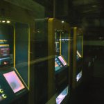 Fileira de terminais de autoatendimento iluminados em um ambiente escuro.