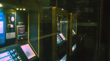 Fileira de terminais de autoatendimento iluminados em um ambiente escuro.