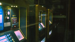 Fileira de terminais de autoatendimento iluminados em um ambiente escuro.