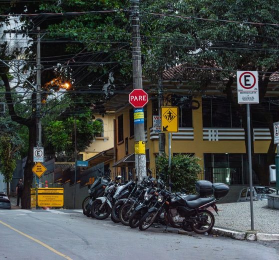 Motocicletas estacionadas em uma rua de Belo Horizonte, diante de placas e sinalização urbana.