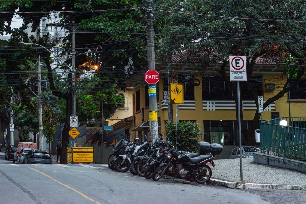 Motocicletas estacionadas em uma rua de Belo Horizonte, diante de placas e sinalização urbana.