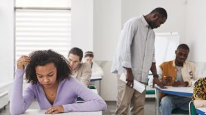 Estudantes realizam uma prova em sala de aula enquanto são supervisionados por um professor.