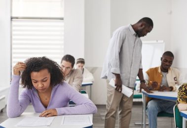 Estudantes realizam uma prova em sala de aula enquanto são supervisionados por um professor.