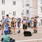 Banda toca instrumentos ao ar livre enquanto anima o público em um espaço público.