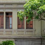 Fachada de uma construção histórica com janelas de madeira, cercada por vegetação em Belo Horizonte.