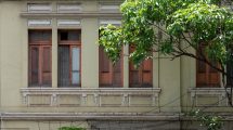 Fachada de uma construção histórica com janelas de madeira, cercada por vegetação em Belo Horizonte.