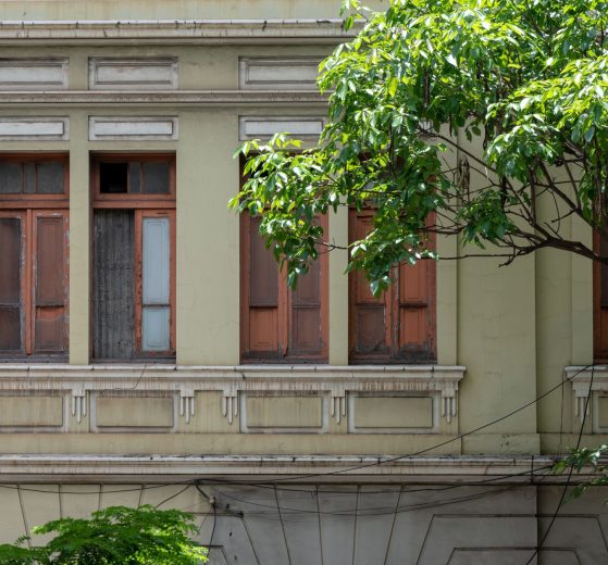 Fachada de uma construção histórica com janelas de madeira, cercada por vegetação em Belo Horizonte.