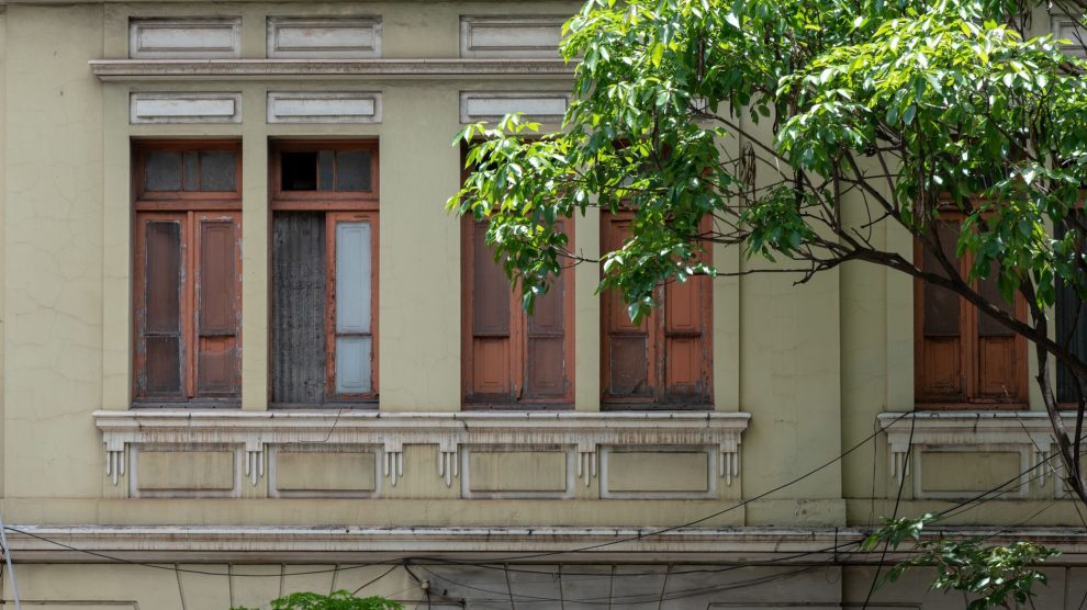 Fachada de uma construção histórica com janelas de madeira, cercada por vegetação em Belo Horizonte.