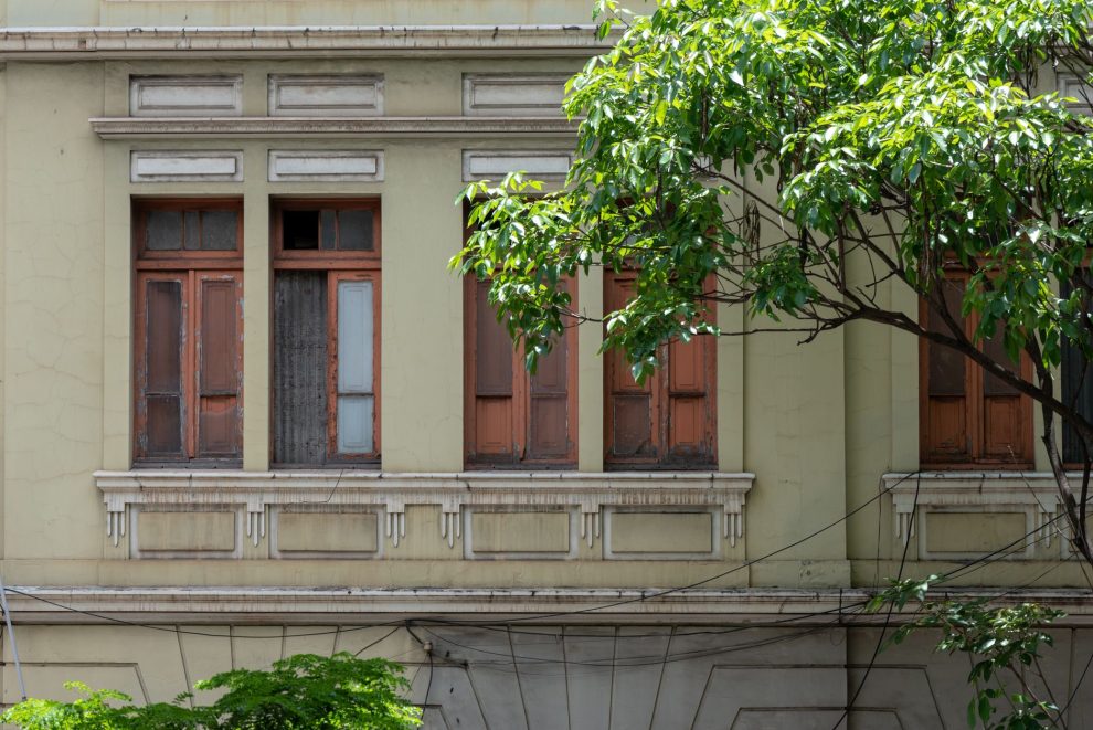 Fachada de uma construção histórica com janelas de madeira, cercada por vegetação em Belo Horizonte.