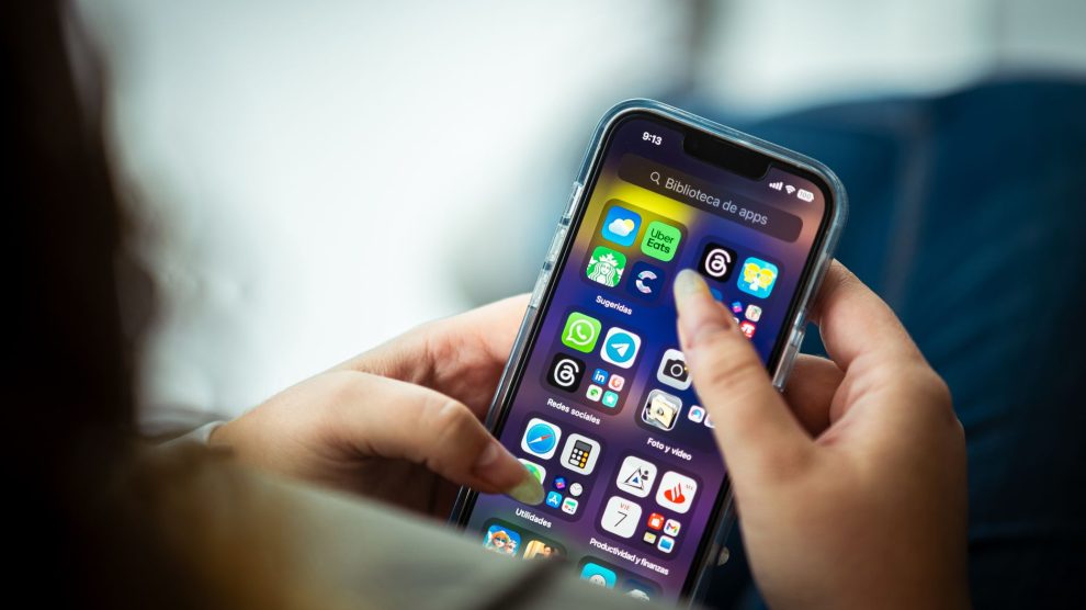 Mulher segura um smartphone que exibe diversos aplicativos.