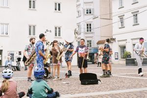 Banda toca instrumentos ao ar livre enquanto anima o público em um espaço público.