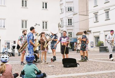 Banda toca instrumentos ao ar livre enquanto anima o público em um espaço público.