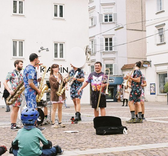 Banda toca instrumentos ao ar livre enquanto anima o público em um espaço público.