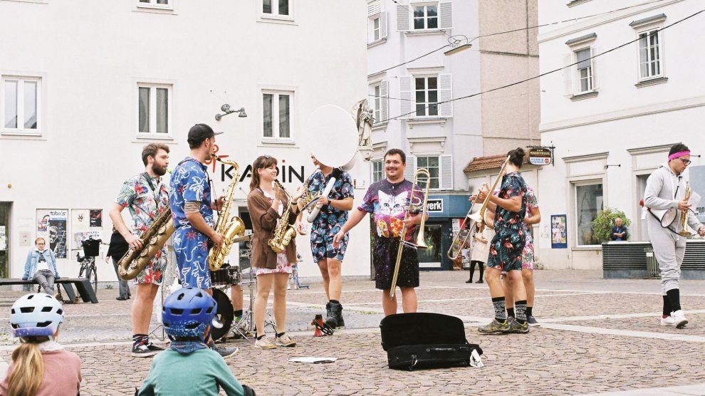 Banda toca instrumentos ao ar livre enquanto anima o público em um espaço público.