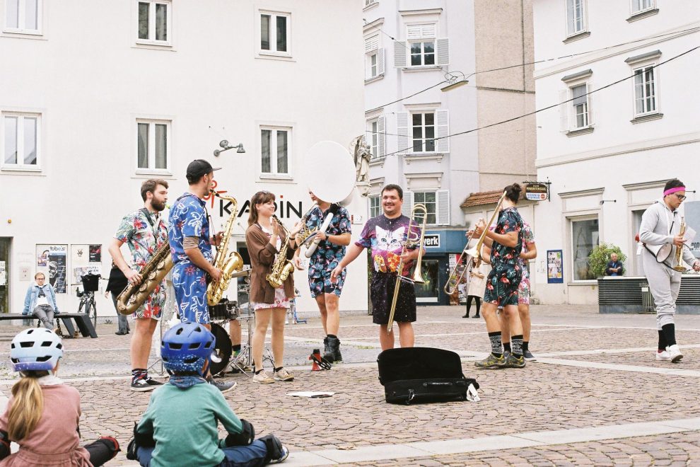 Banda toca instrumentos ao ar livre enquanto anima o público em um espaço público.